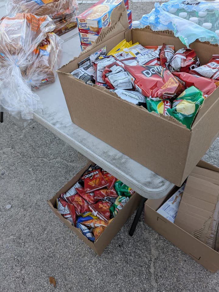 Boxes of chips and snacks beside loaves of bread and bottled water on a serving table