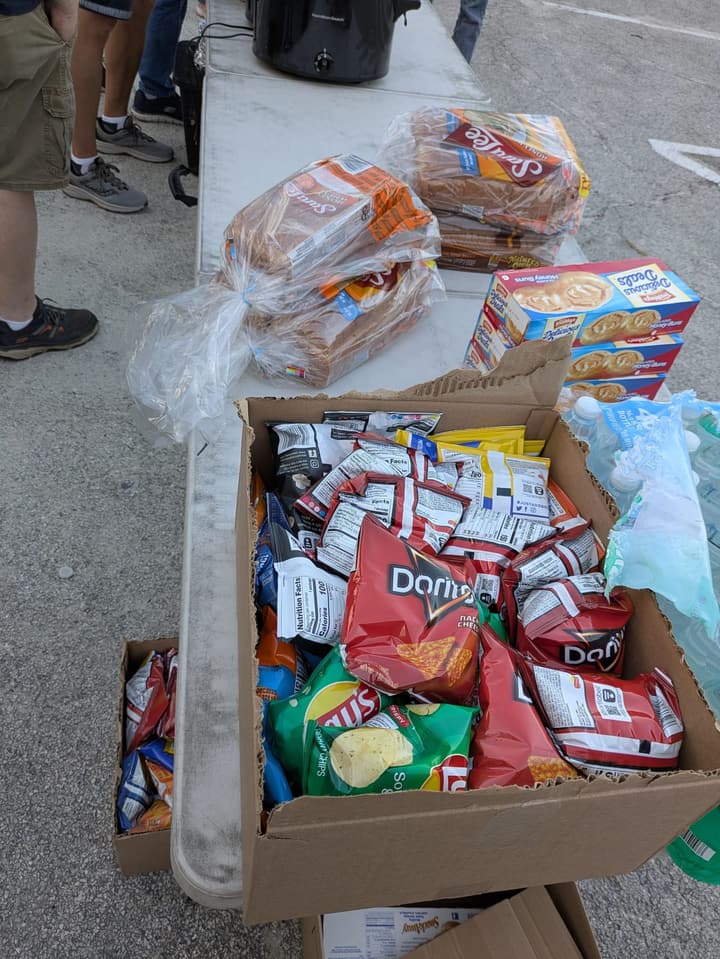 Serving table stocked with loaves of bread, snack cakes, a box of chips and bottled water