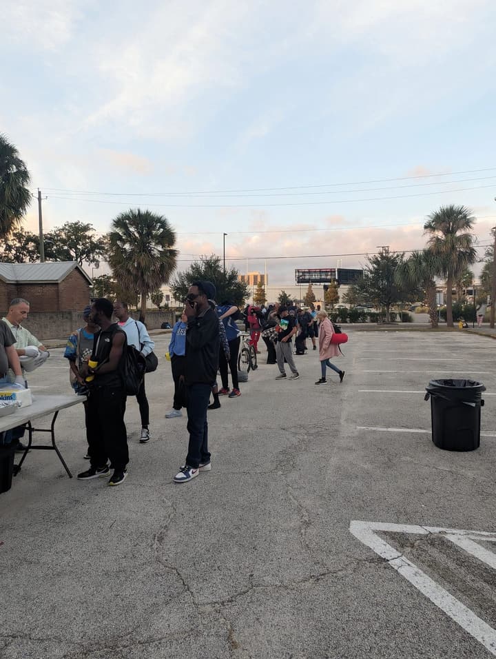 People line up beside the serving table as evening falls over the parking lot