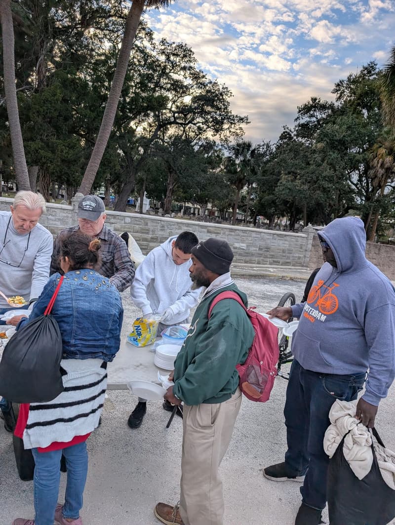 Volunteers spoon hot food onto plates for people waiting at the serving table
