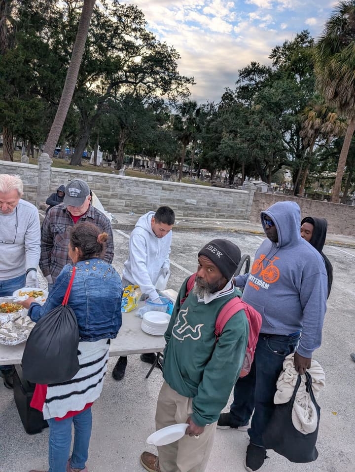 A volunteer fills a plate with hot food while people hold plates and wait their turn