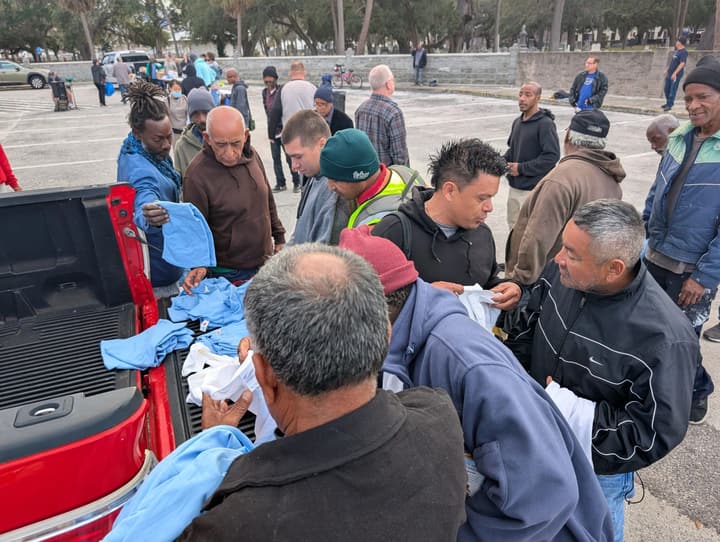 People gather at a pickup's tailgate to choose from donated blue and white T-shirts