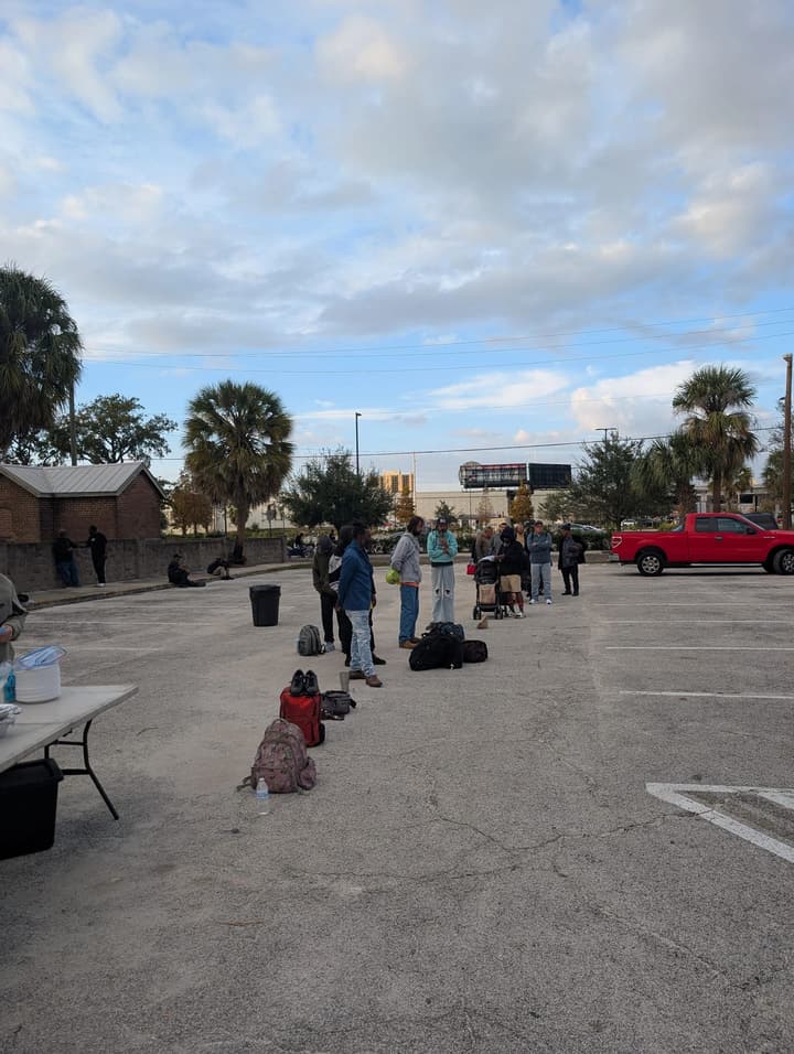 People wait in line across the parking lot under a cloudy evening sky
