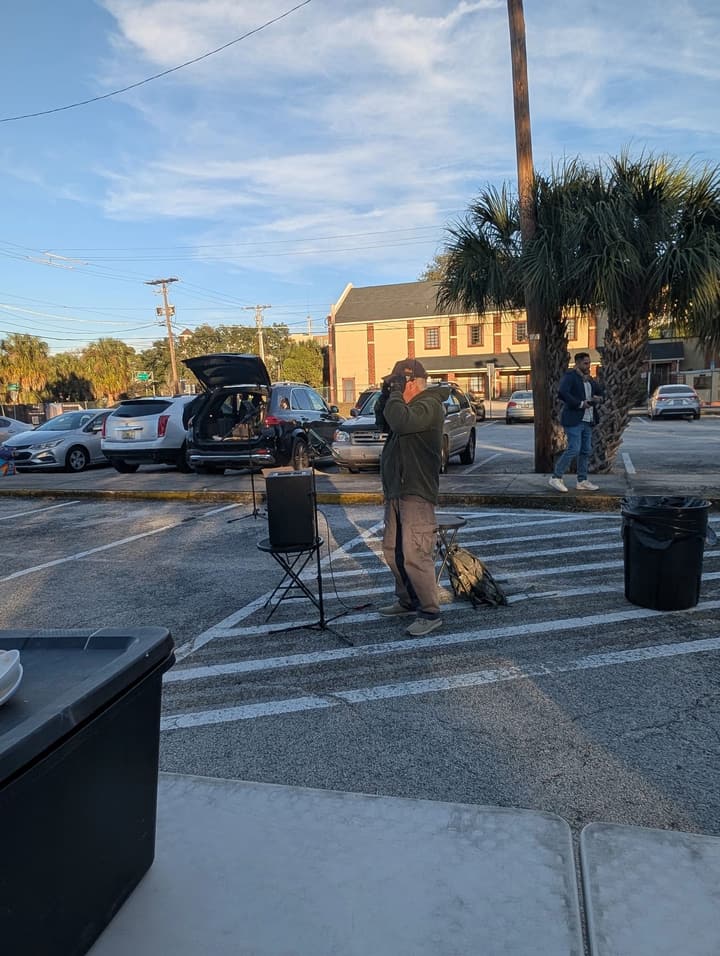 A musician adjusts his headset microphone beside a speaker set up in the parking lot