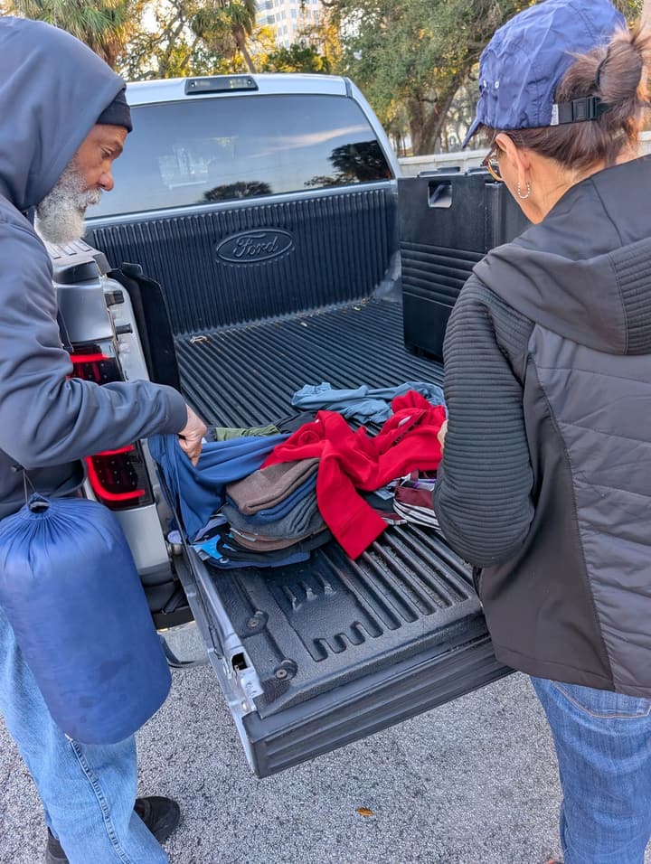A volunteer and a man look through donated clothing on a pickup truck's tailgate