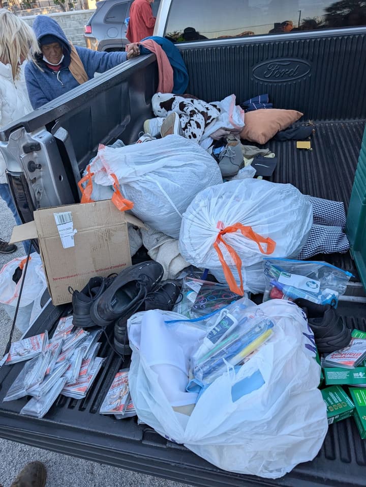 Donated shoes, bagged clothing, toiletries and a pillow fill a pickup truck bed for giving away