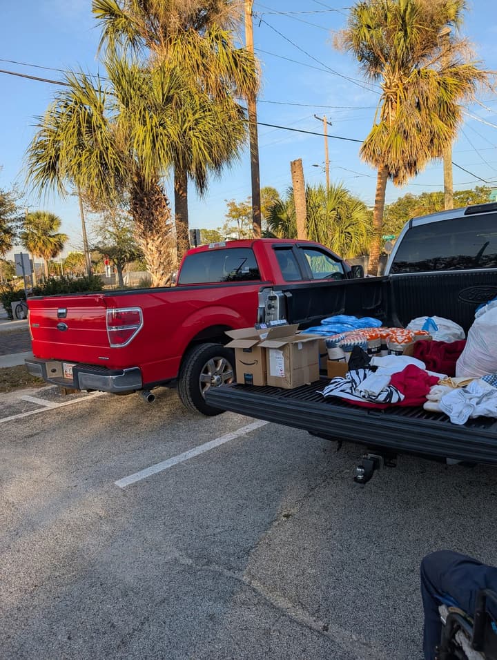 Boxes of supplies and donated clothing laid out on a pickup's tailgate beneath palm trees