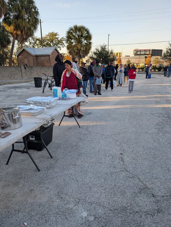 People line up in the golden evening light while a volunteer waits at the serving table