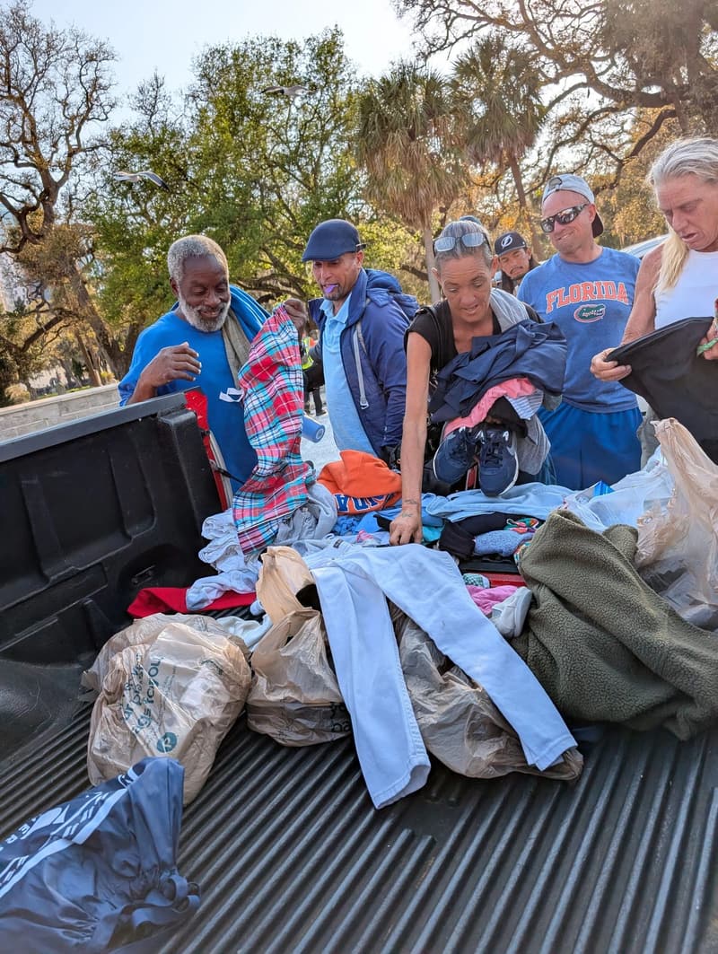People smile as they look through donated clothing and shoes in the bed of a pickup truck